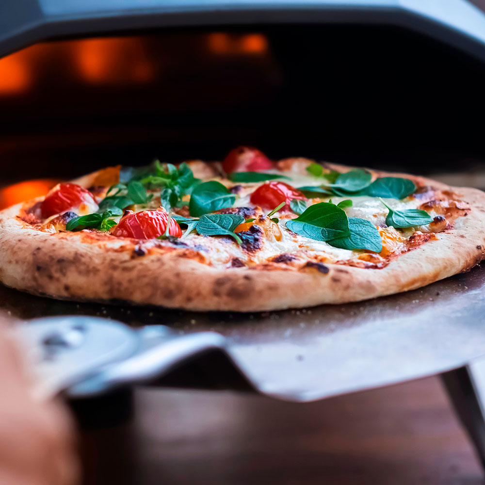 Friskbagt pizza med sprød skorpe, toppet med smeltet mozzarella, saftige cherry-tomater og friske basilikumblade. Pizzaen bliver løftet ud af en varm ovn.